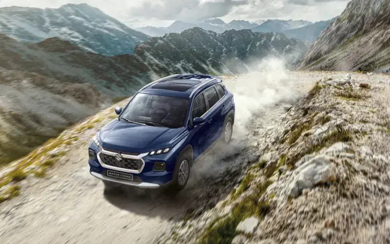 SUV Híbrido Grand Vitara azul oscuro conduciendo por un camino de montaña rocoso.