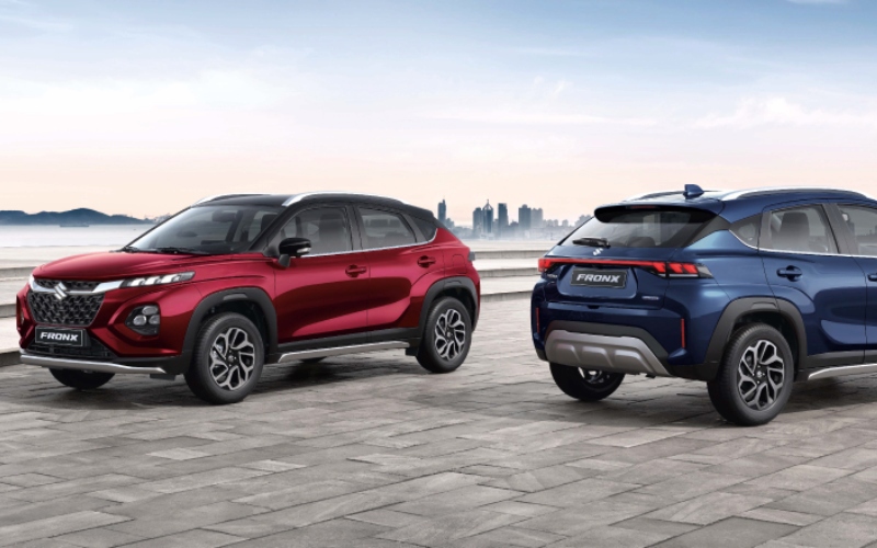 Autos Suzuki Fronx Smart Hybrid rojo y azul con ciudad citadina de fondo