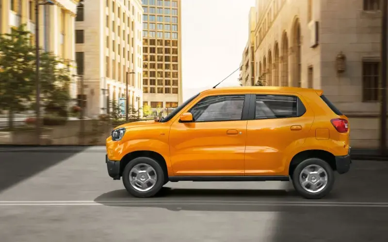 Vista lateral del Suzuki S-Presso naranja, destacando su altura elevada en un entorno urbano.